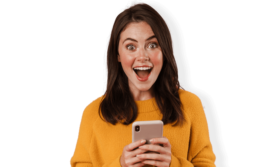 Girl in orange sweater smiling and looking shocked at her phone.
